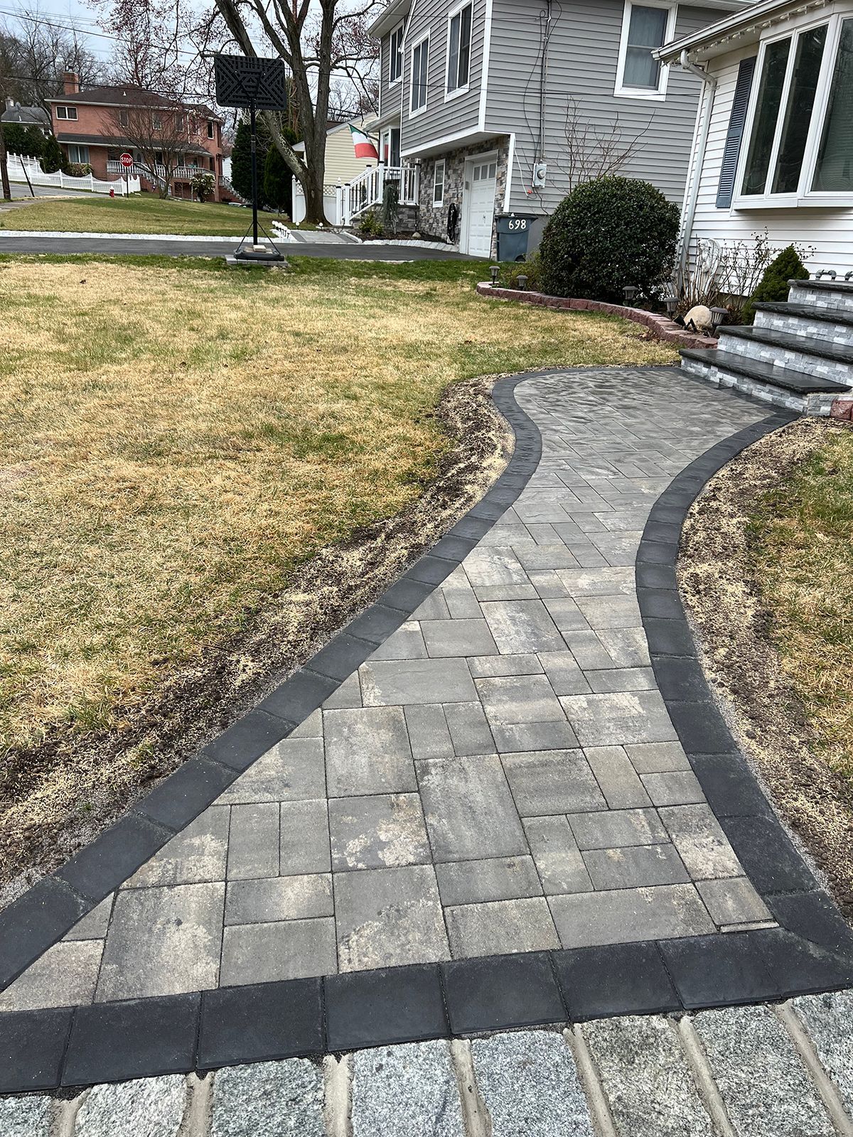 Brick pathway leading to a house with a gray exterior, bordered by grass and dark edging.