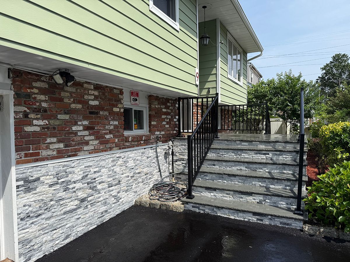 House exterior with brick and stone facade, steps with black railings.