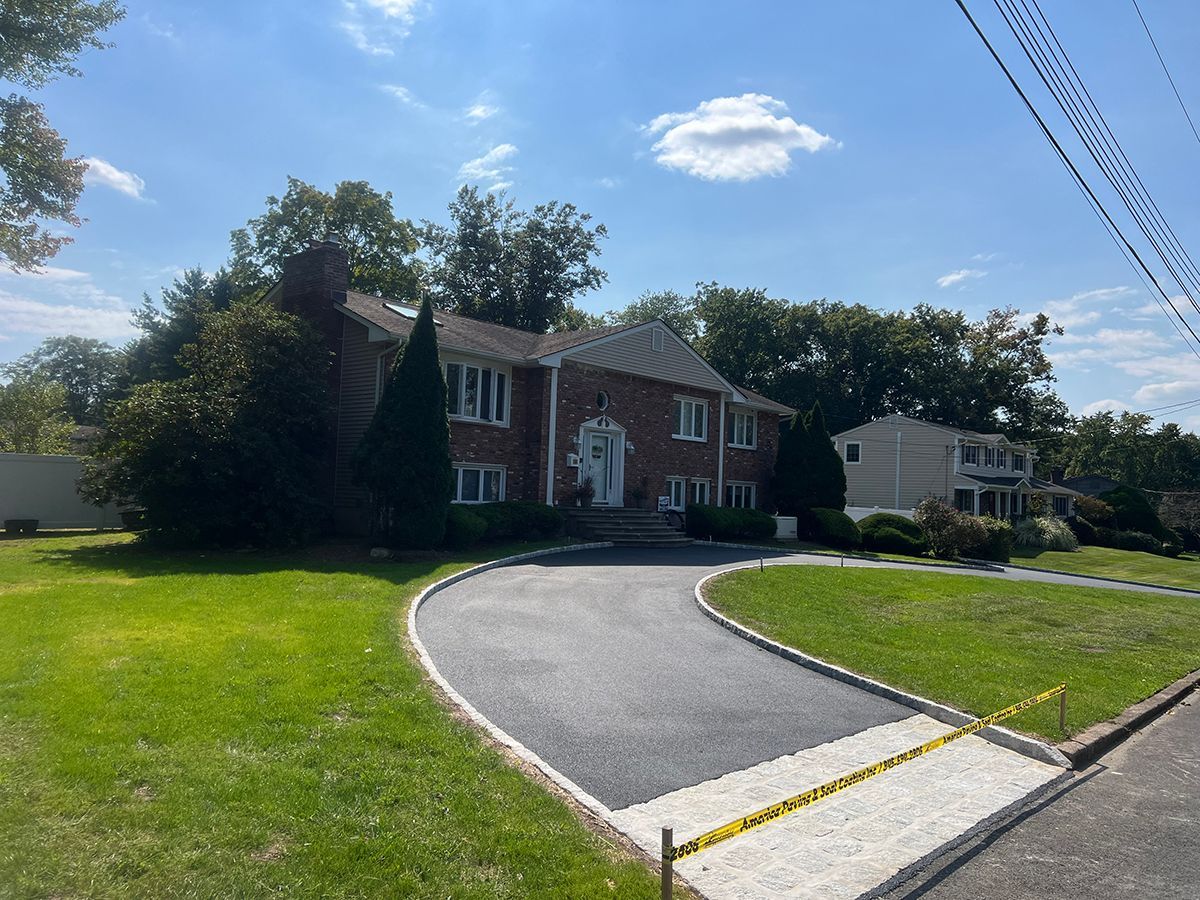 A two-story brick house with a newly paved driveway on a sunny day.