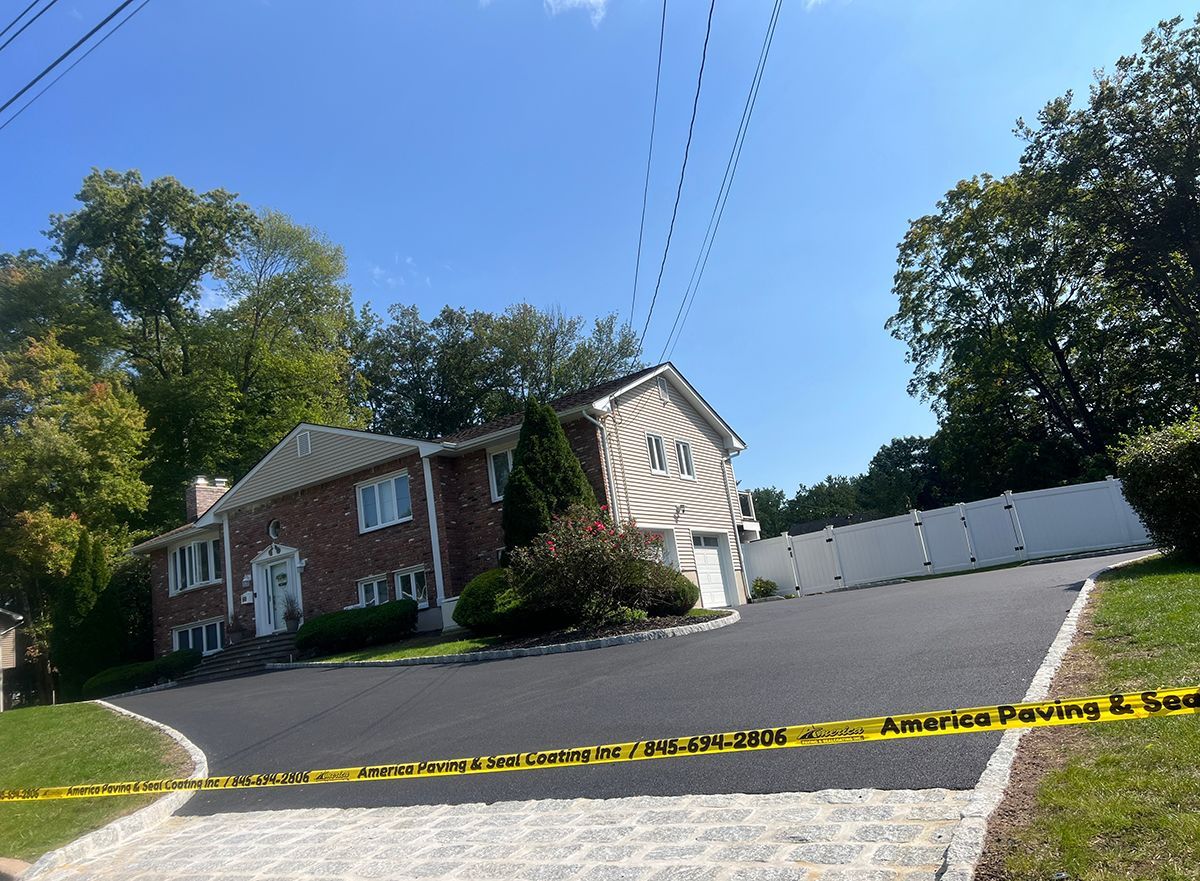 House with a brick facade and a long driveway, seen from a slightly elevated position on a sunny day. Yellow caution tape is across the bottom.