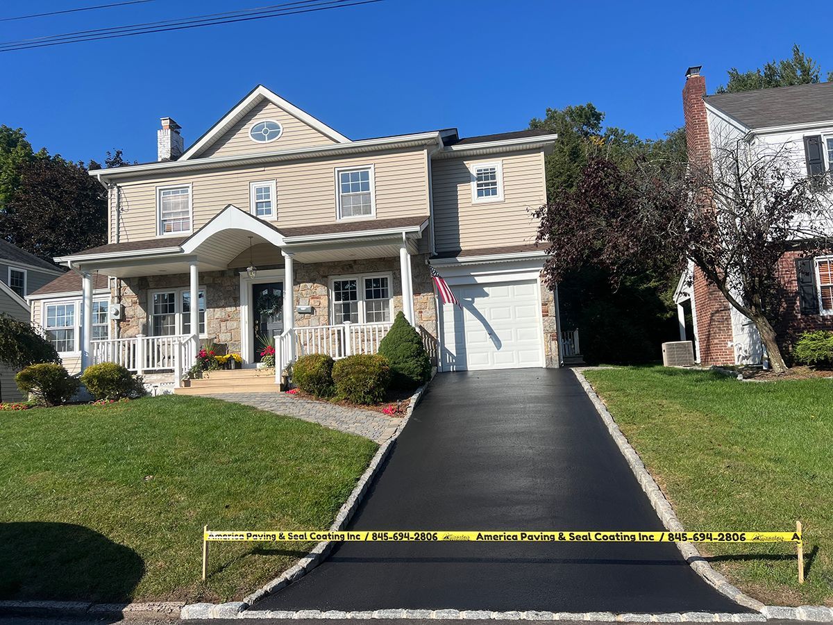 Two-story house with newly paved black driveway; caution tape in foreground.