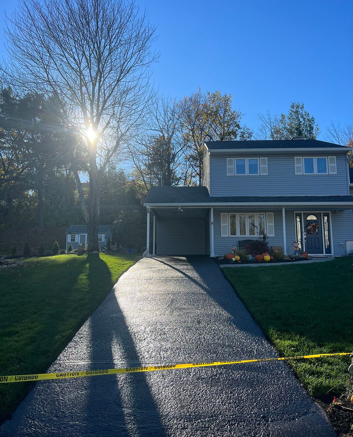House with freshly paved driveway on a sunny day; yellow caution tape in foreground.