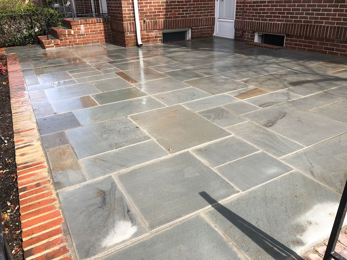 Brick-lined stone patio with various sized rectangular gray stones, next to a brick wall.