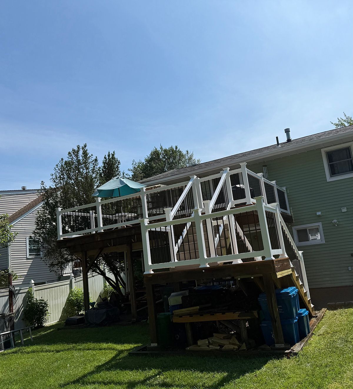 Wooden deck with white railings attached to a light green house. Blue sky overhead.