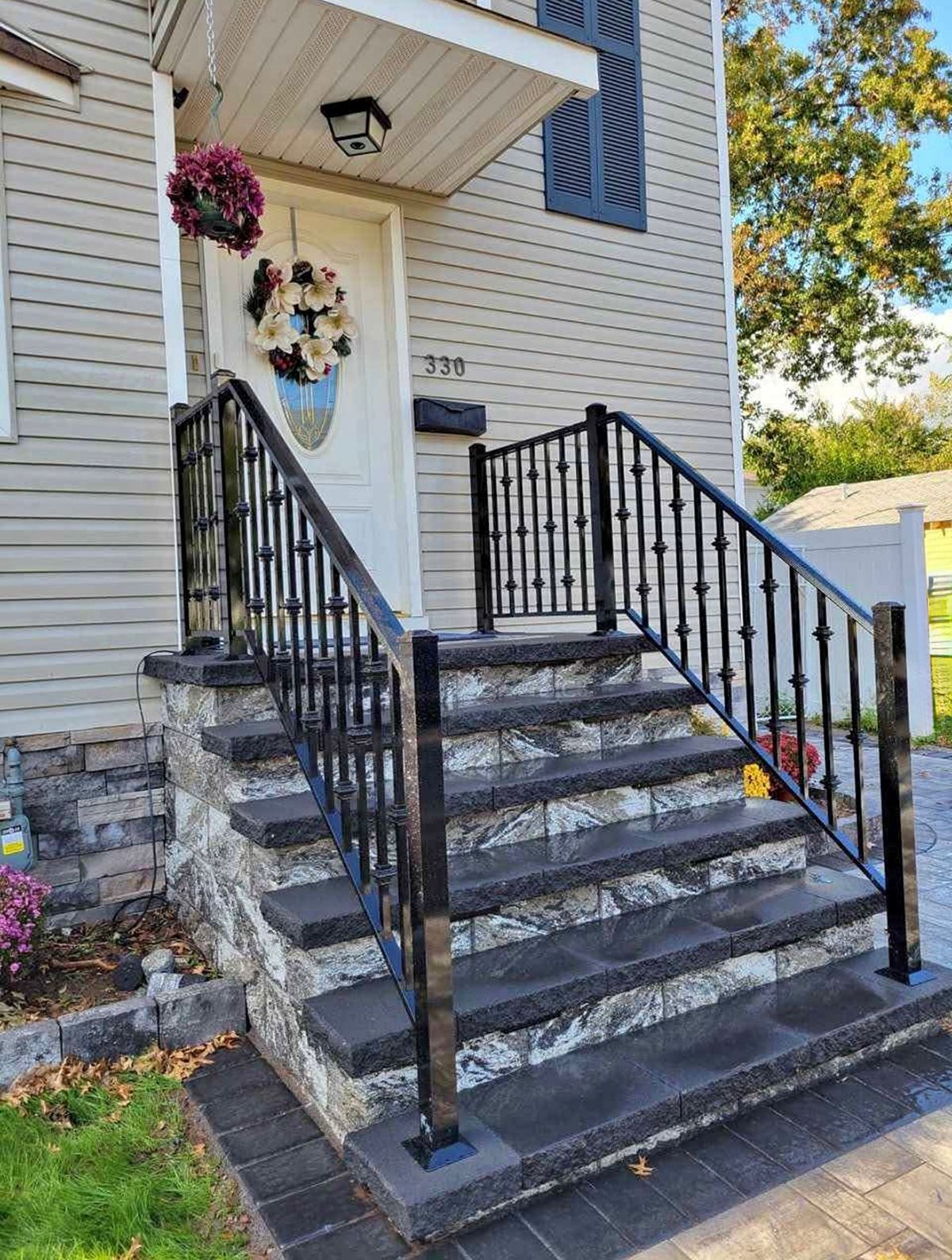 Stone steps lead to a house with black metal railings.  The white door has a wreath.