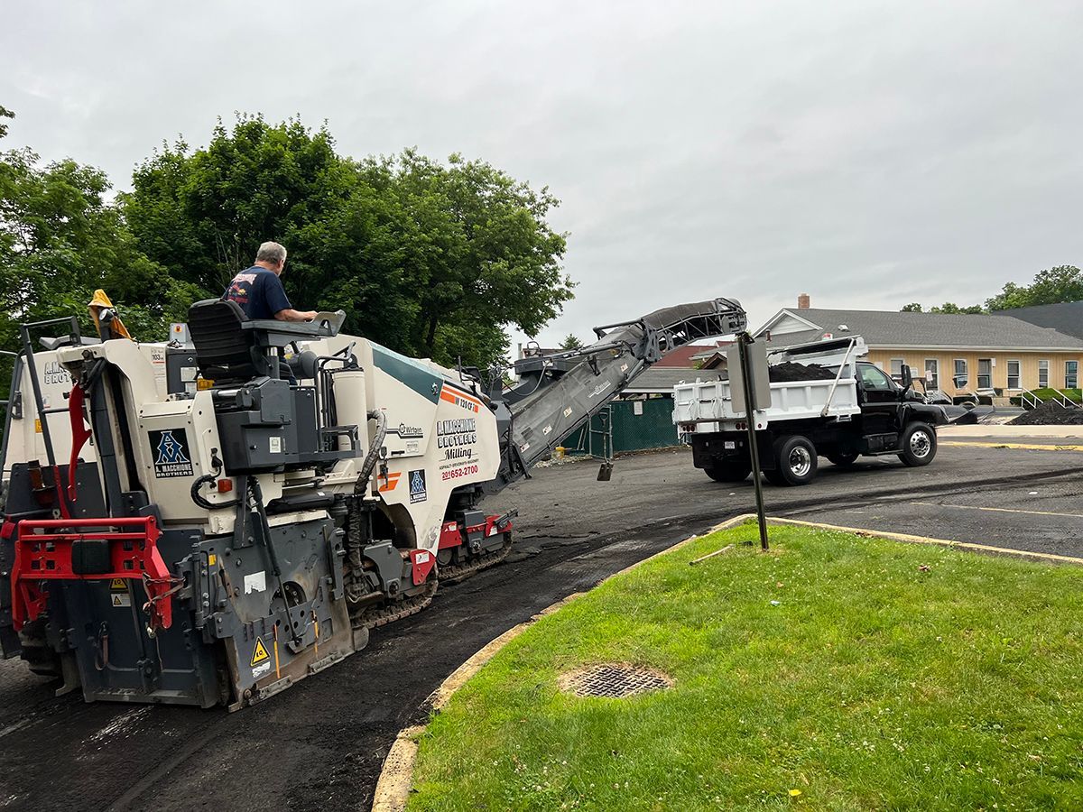 Asphalt milling machine removing pavement, loading dump truck at a construction site.