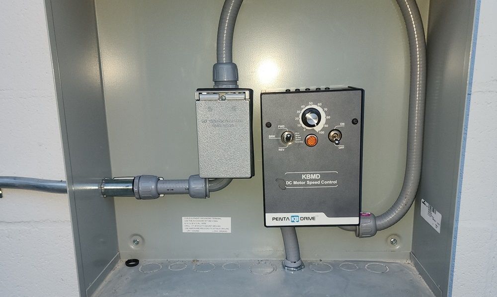 Electrical control panel and junction box mounted in a gray metal cabinet with conduit pipes.