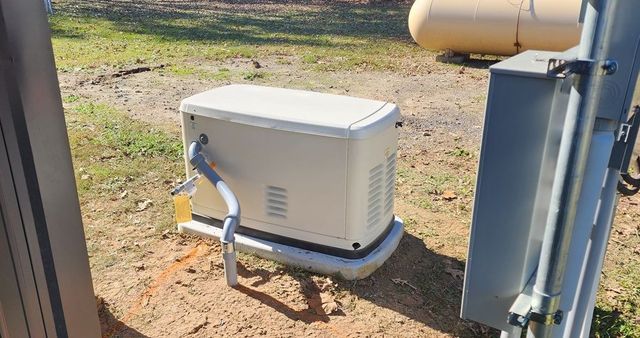 White generator on concrete pad beside metal utility equipment in a grassy outdoor area