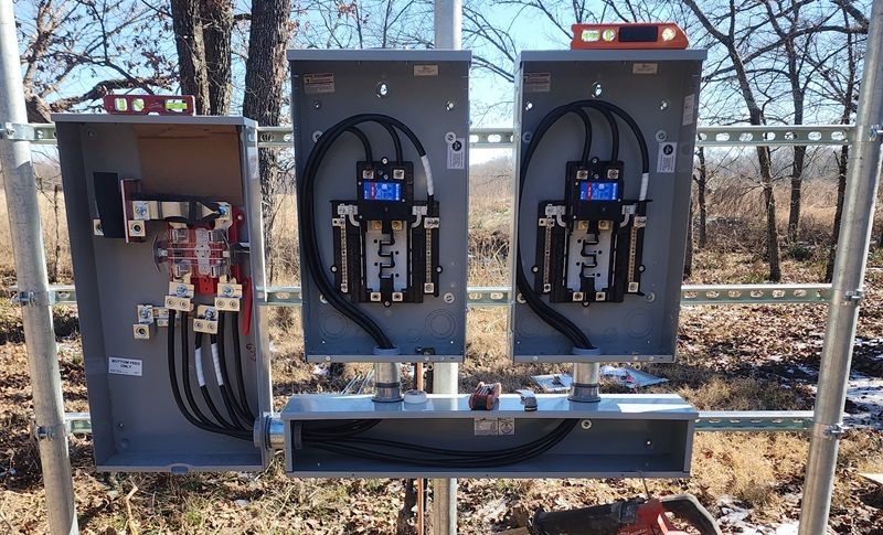 Three electrical service cabinets and meters beside a chain-link fence outdoors