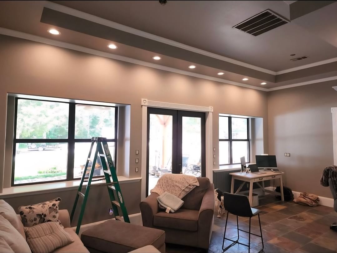 Living room under renovation with ladders, furniture, and drop cloths beneath recessed ceiling lights
