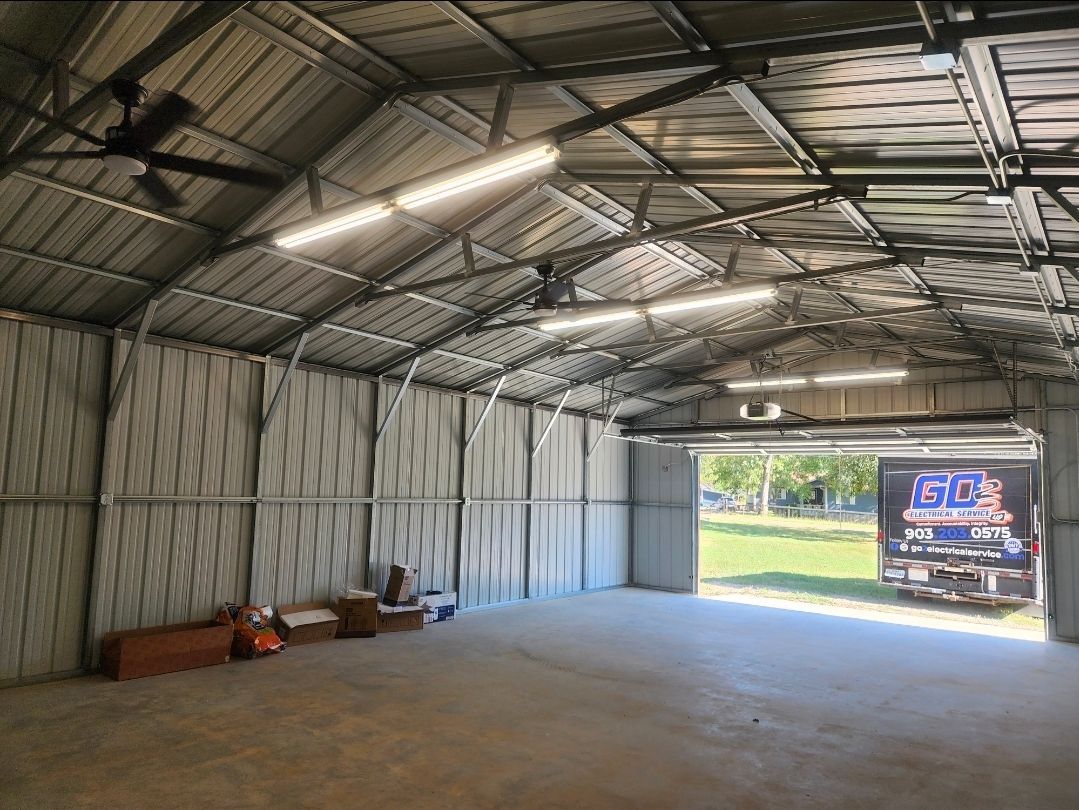Empty metal garage interior with concrete floor, open front, and a truck visible outside.