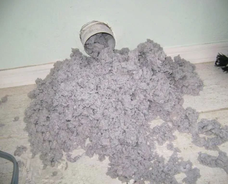 A pile of lint is on the floor next to a pipe