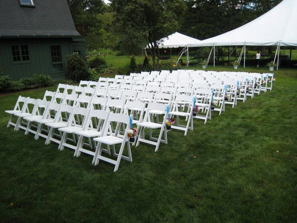 a row of white folding chairs in a grassy field