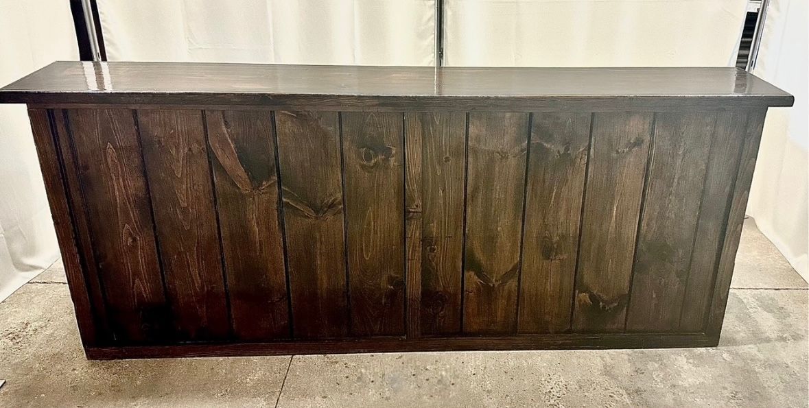 A wooden table is sitting on a concrete floor in front of a white curtain.