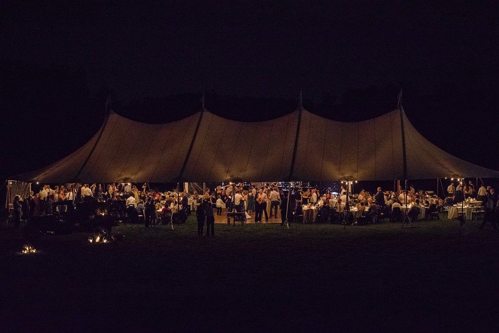 a large tent is lit up at night with people standing underneath