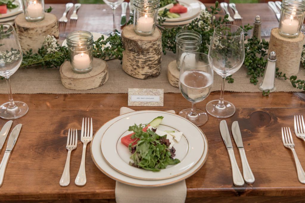 a wooden table with plates , silverware , candles and a salad on it