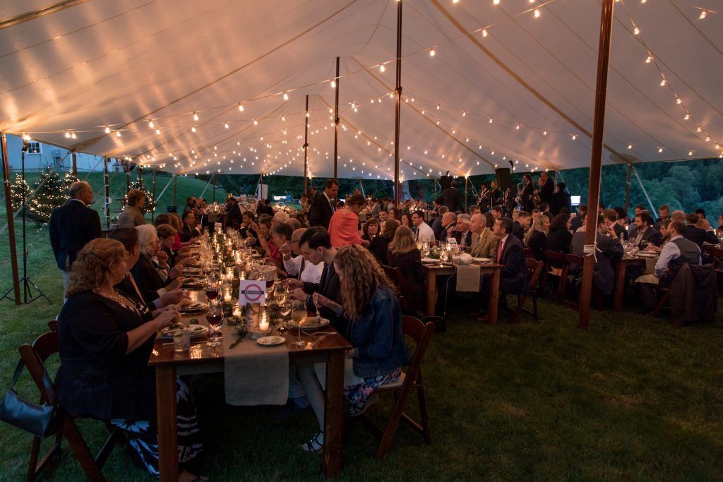 a large group of people are sitting at long tables under a tent
