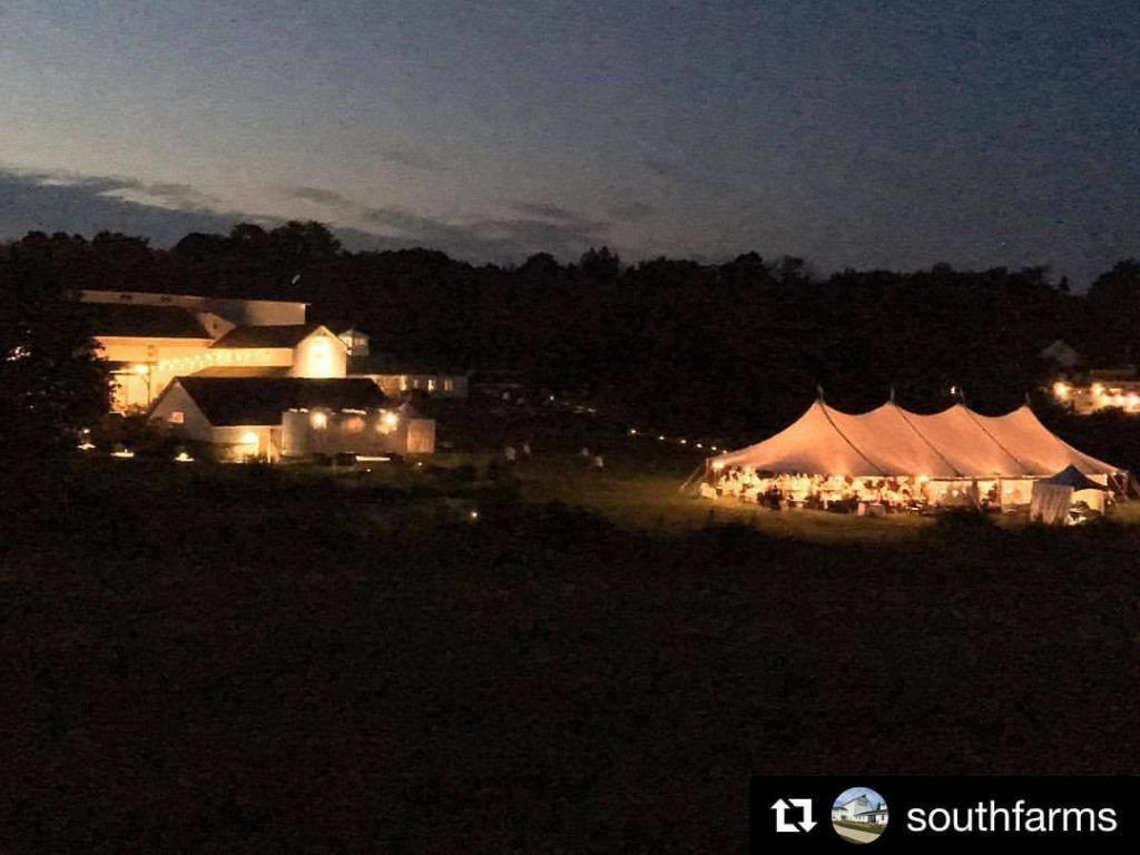 a large tent is lit up in front of a barn at night