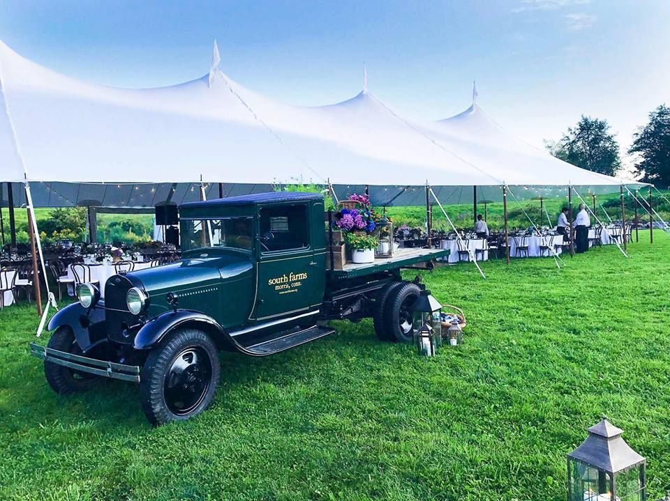 an old truck is parked in a grassy field under a white tent