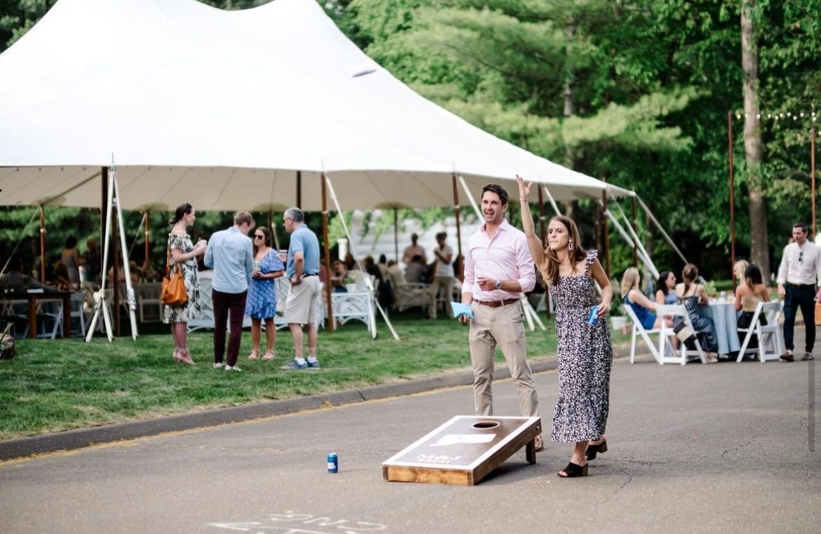 a man and a woman are playing cornhole under a tent