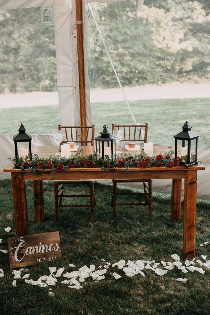 a wooden table with lanterns and flowers on it in a tent