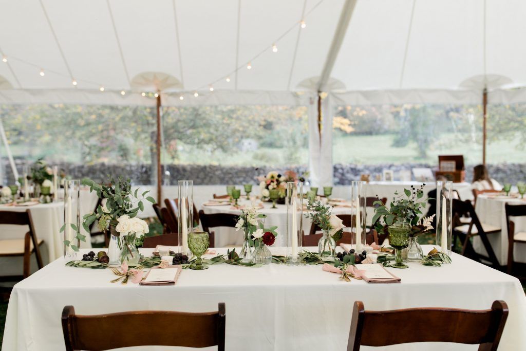 a long table with a white tablecloth and wooden chairs in a tent