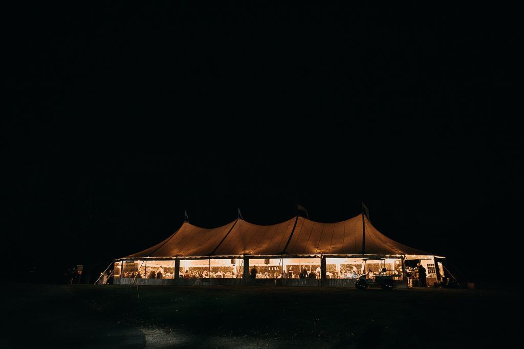 a large tent is lit up at night in the middle of a field