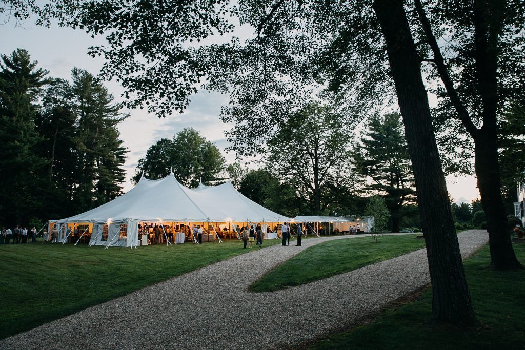 a large white tent is sitting in the middle of a field surrounded by trees