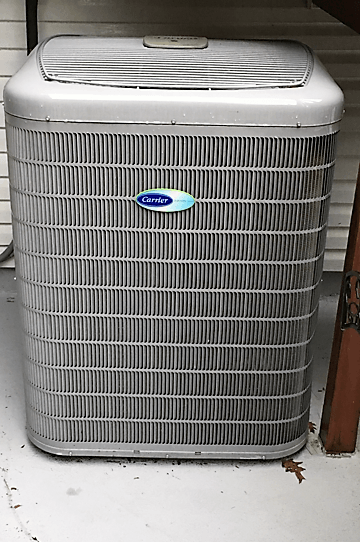 A carrier air conditioner is sitting on the floor next to a door.