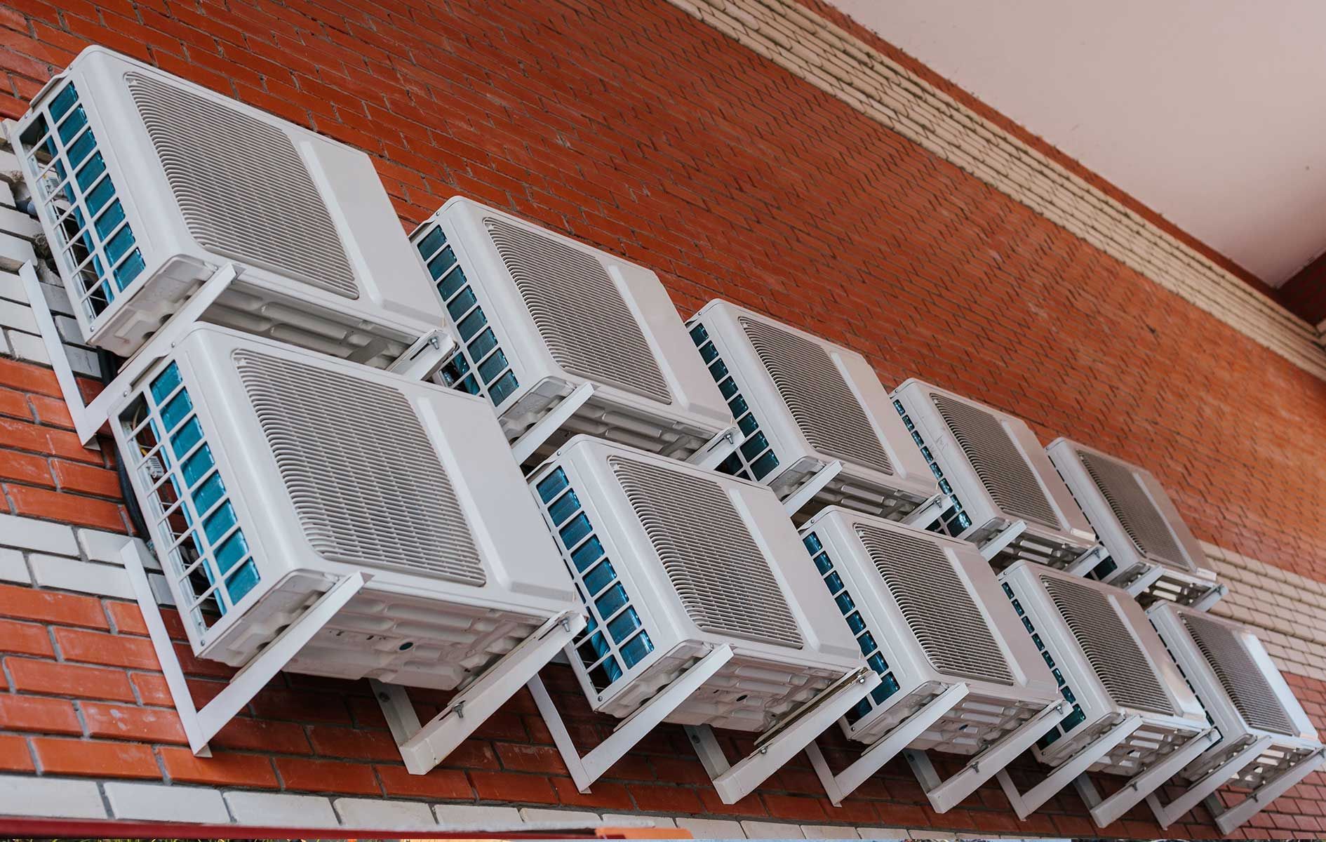 A row of air conditioners are stacked on top of each other on a brick wall. l