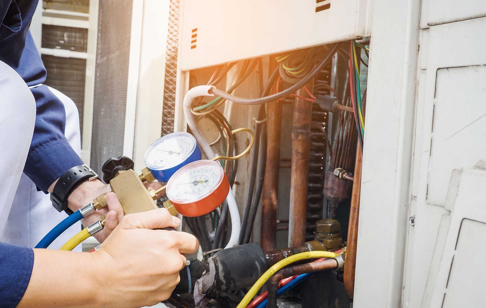 A man is working on an air conditioner with a vacuum gauge.