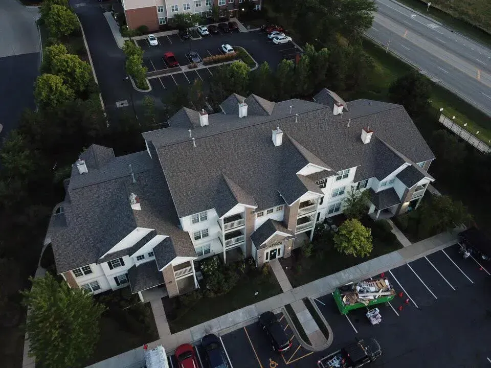 Aerial view of a multi-story apartment building with a gray roof and surrounding parking lot.