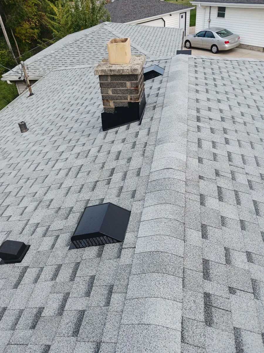 Gray asphalt shingle roof with chimney and two black vents. A car is parked in the background.
