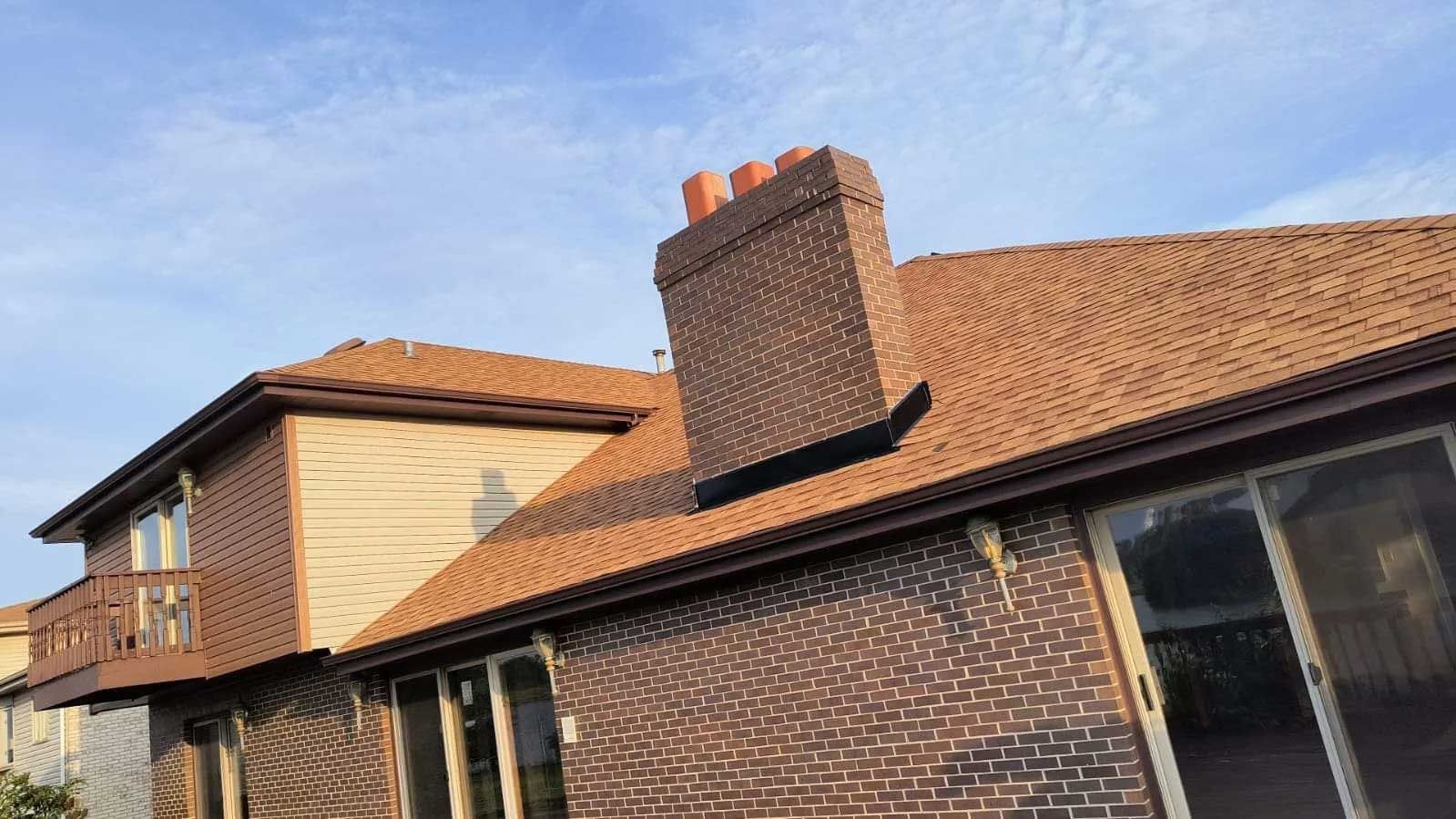 Brick house with brown roof and chimney against a blue sky.