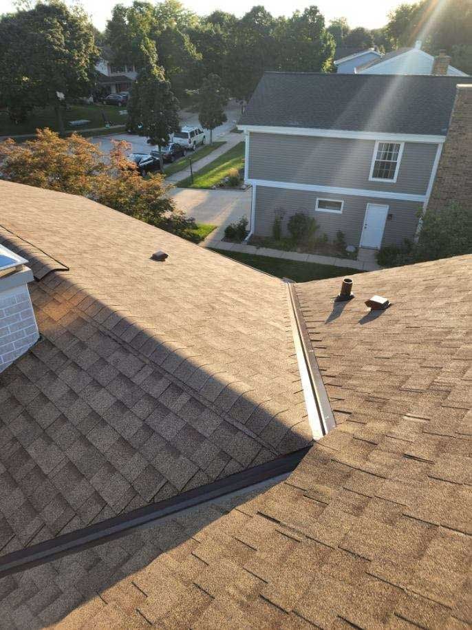 Brown shingled roof with a building and street in the background on a sunny day.