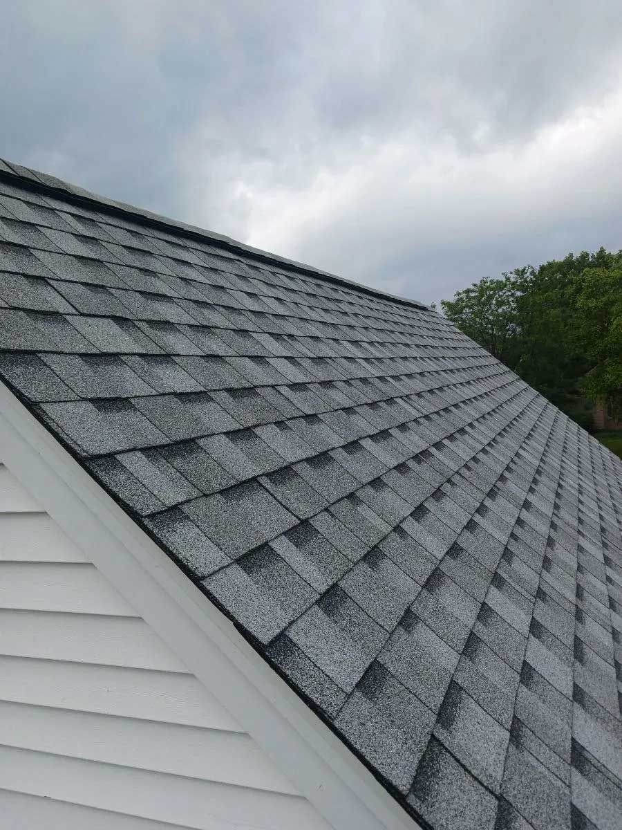 Gray asphalt shingle roof on a house with white siding, set against a cloudy sky.