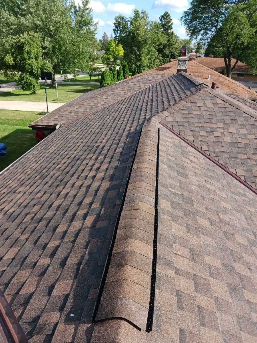 Brown shingle roof with a central ridge vent, trees in the background.