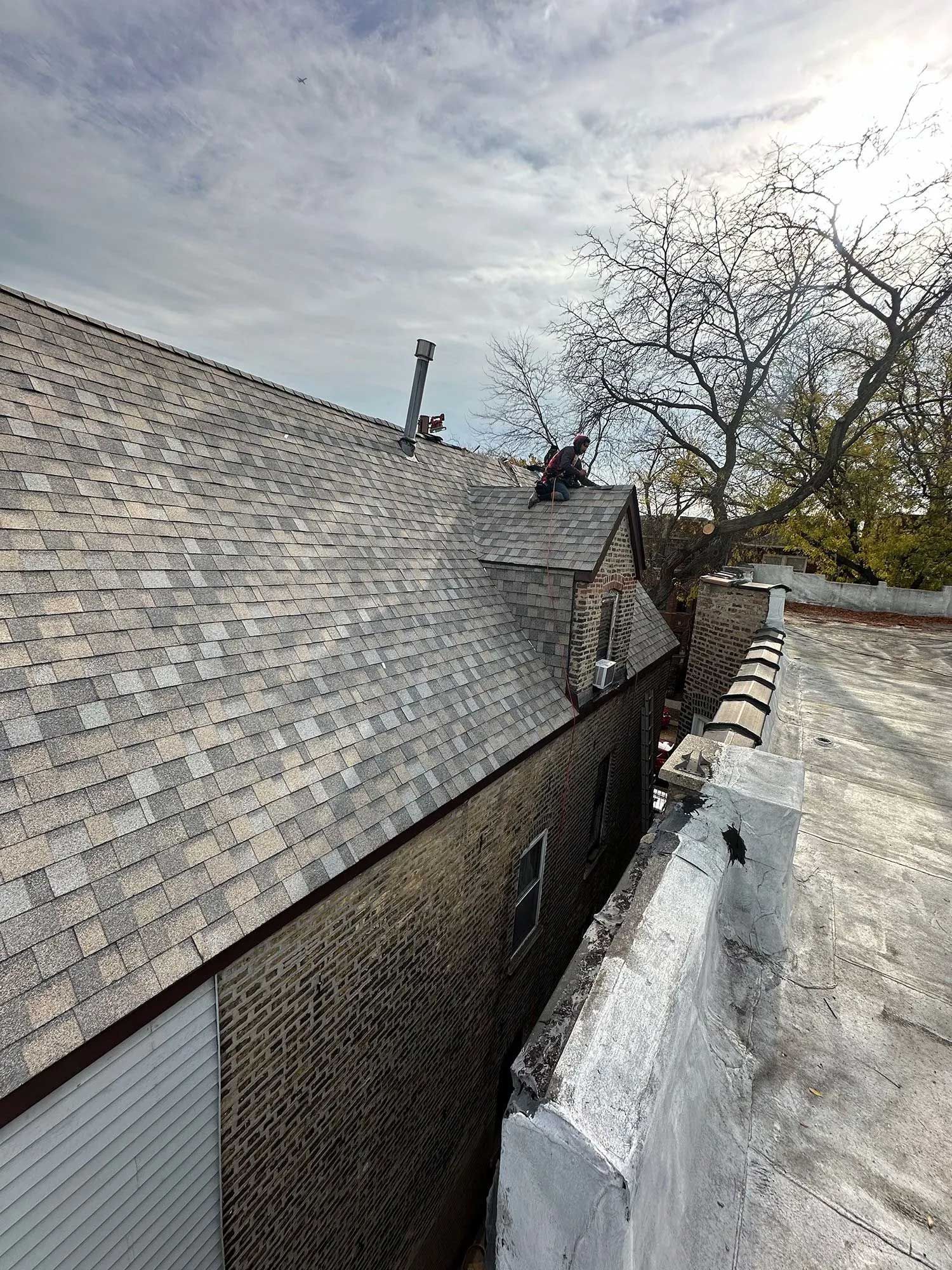 Damaged shingle roof with missing sections. Brick building next to a flat roof. Cloudy sky.