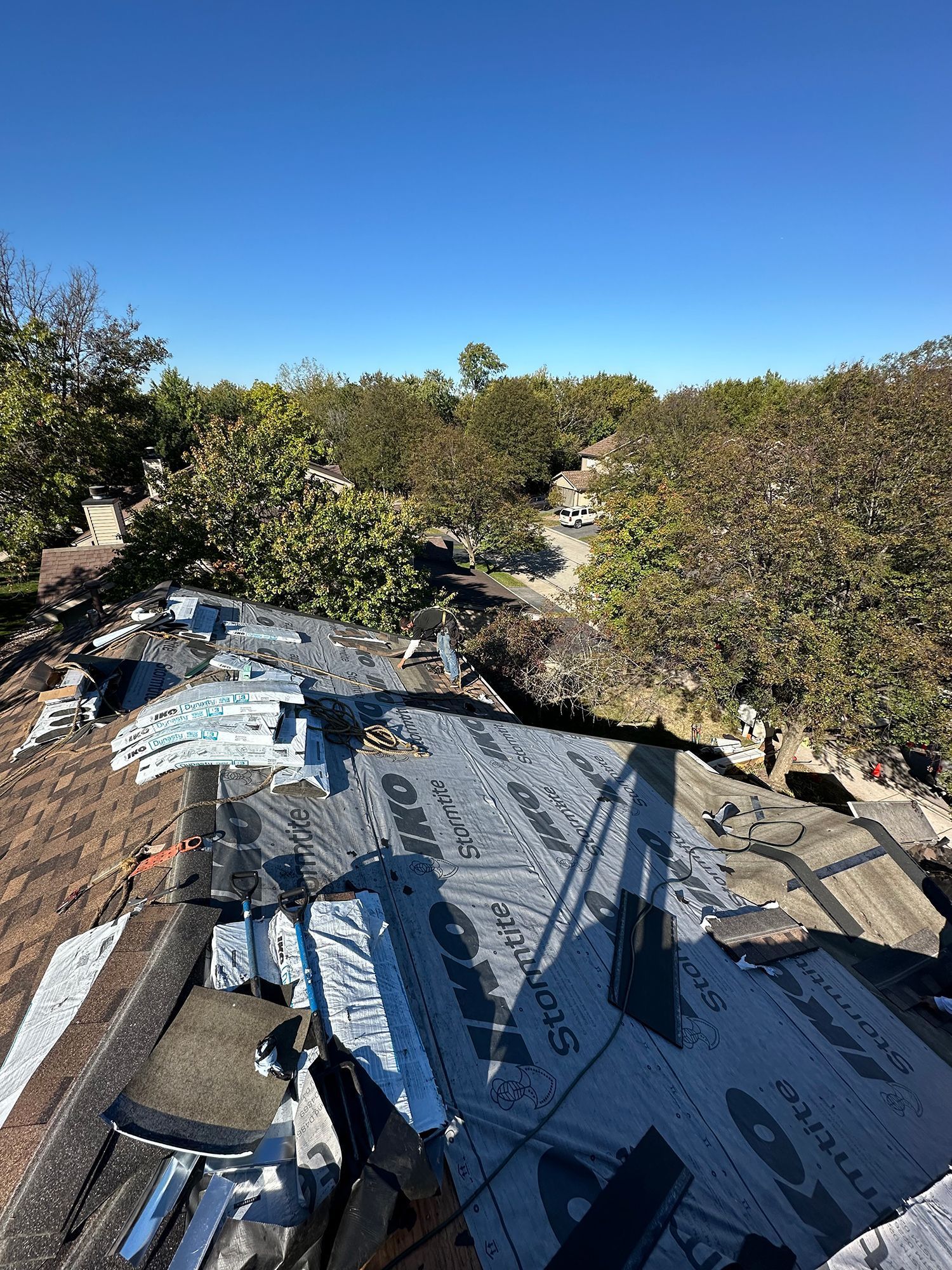 Partially re-roofed house with trees in the background under a blue sky.