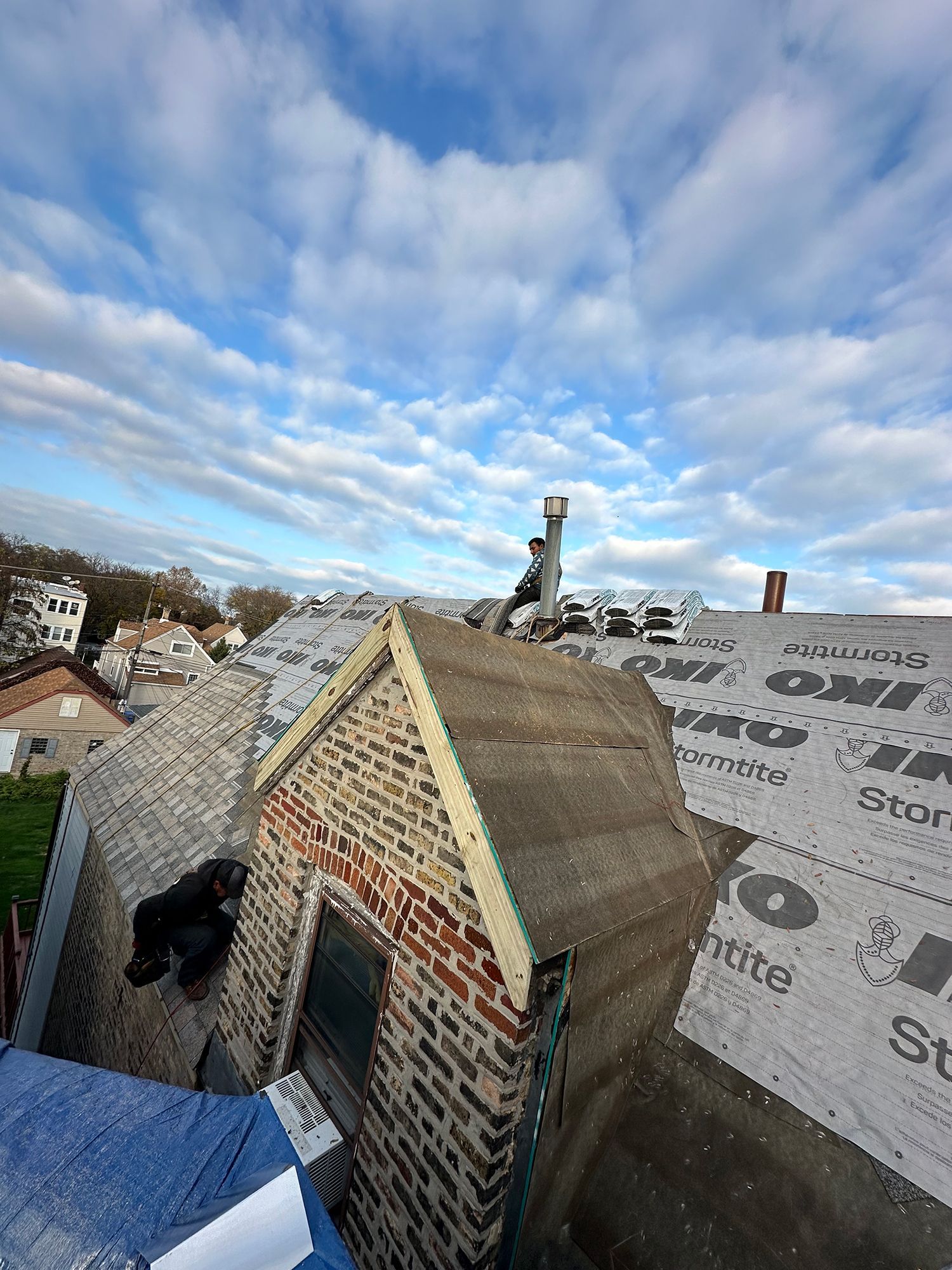 Rooftop view of a building under construction. A person works near a chimney. Cloudy sky.