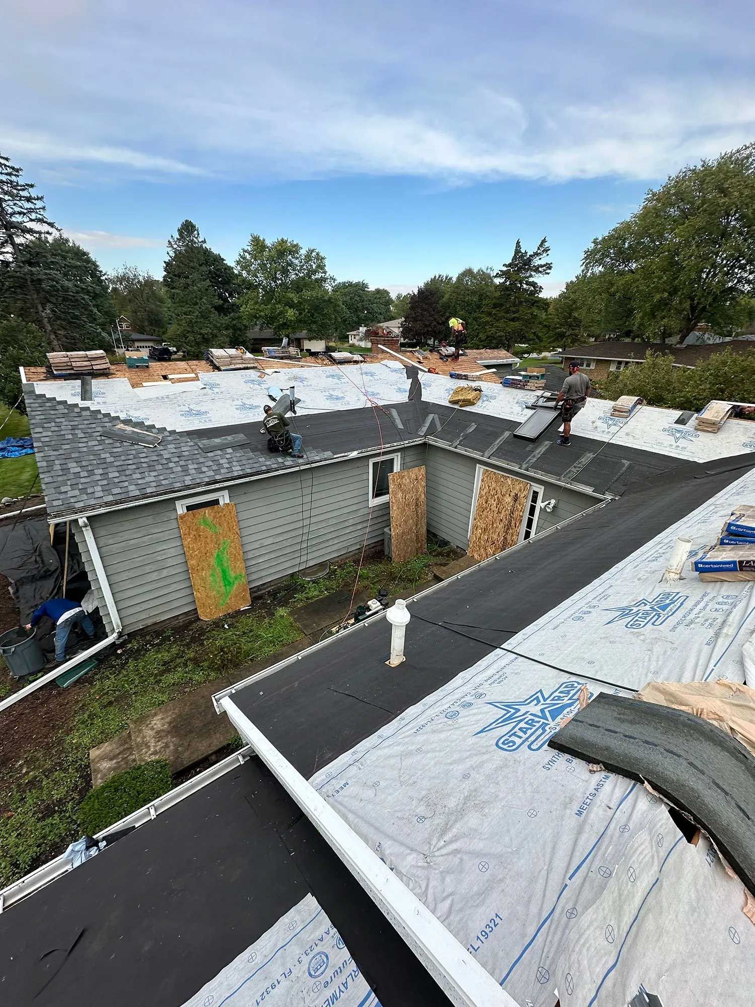 Roofers working on a residential roof with old shingles being removed and new underlayment installed. Cloudy sky.