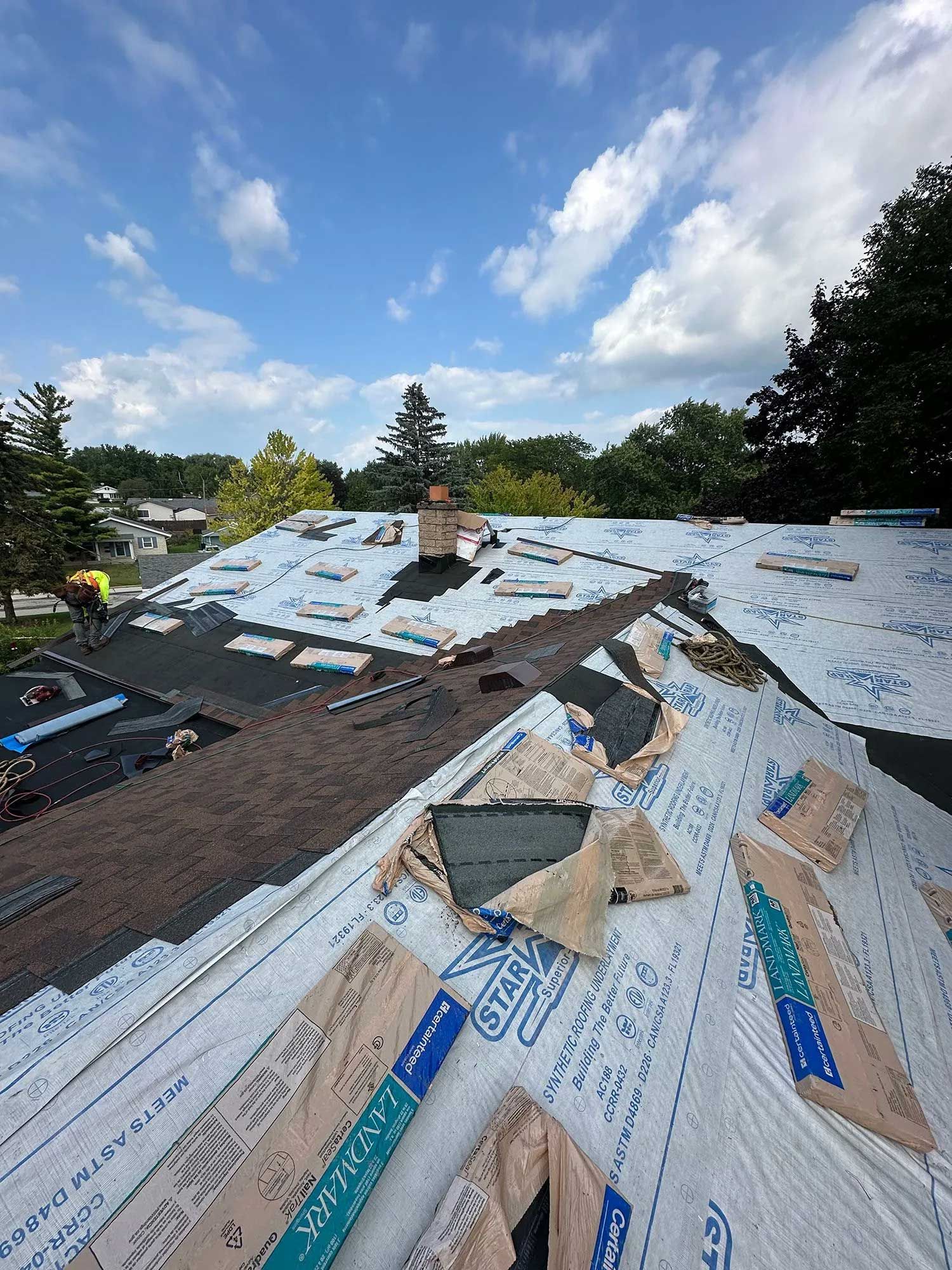Roof replacement in progress on a sunny day. Overlapping roofing material and blue sky are visible.