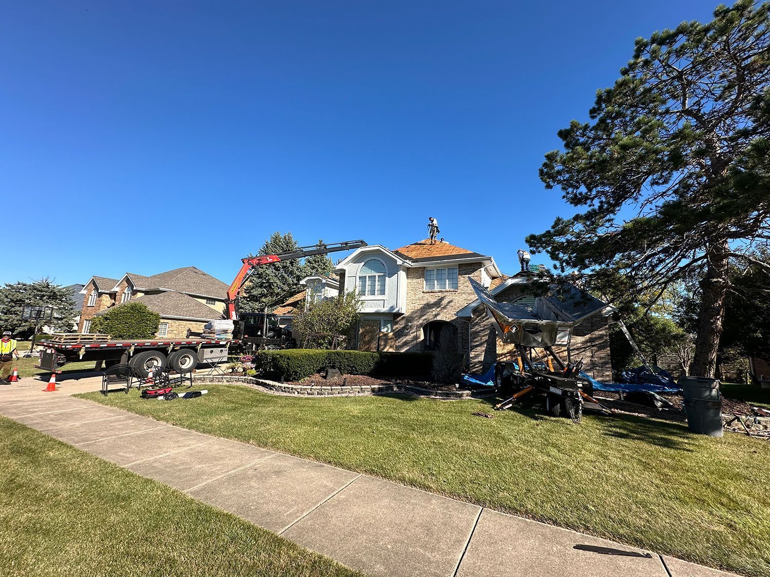 House under construction; stone facade, blue sky, tools and flatbed truck on lawn.