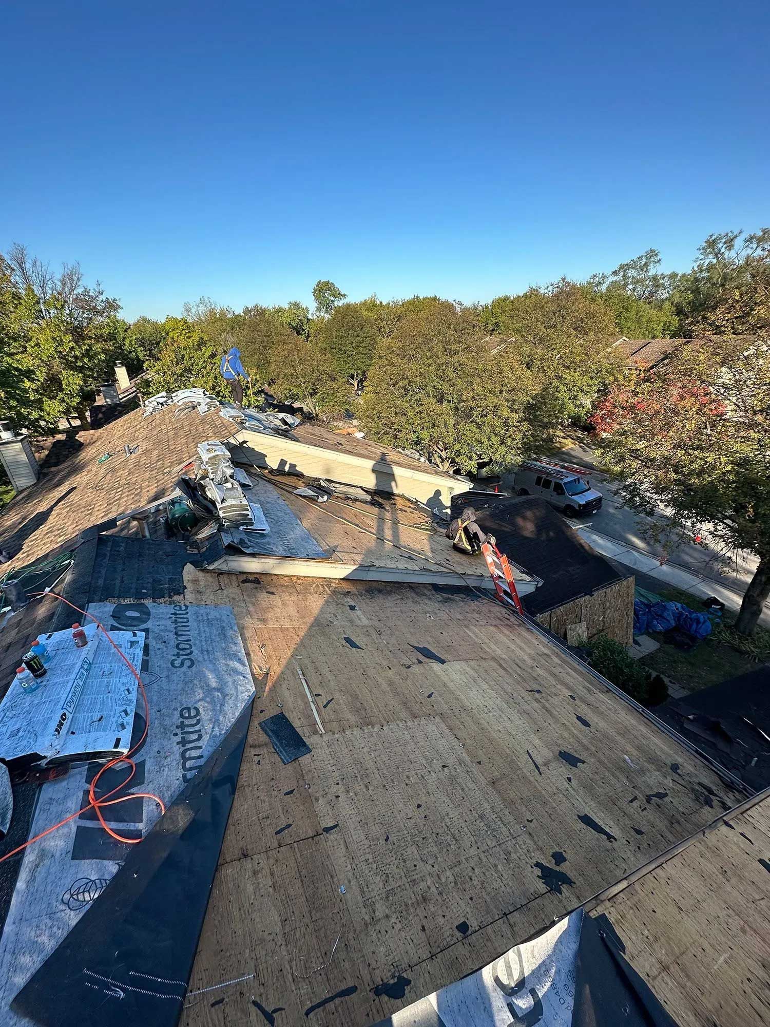 Roof under construction; debris pile on top, worker, trees, blue sky.