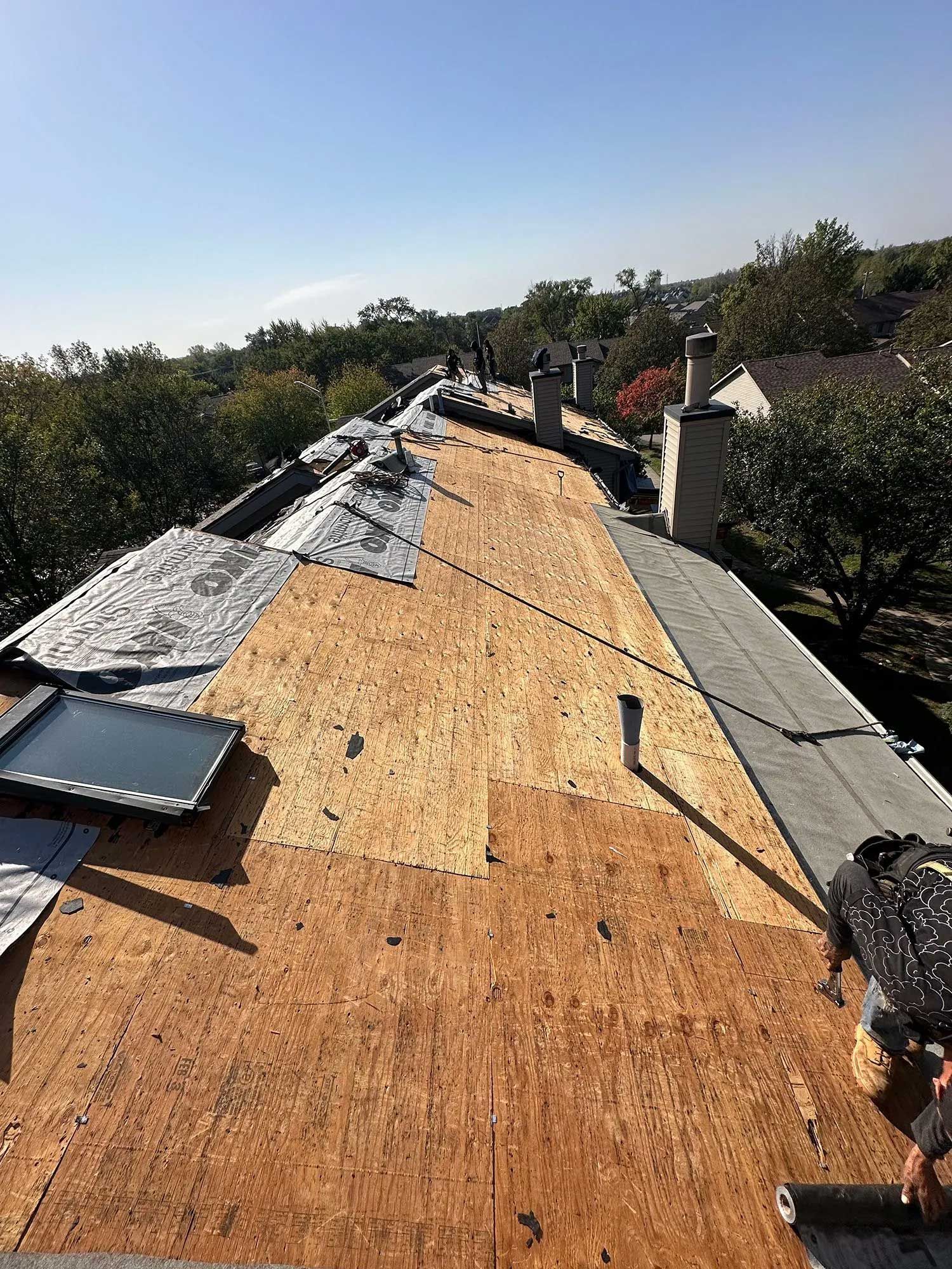 Roof under construction with exposed wood and workers on a sunny day.