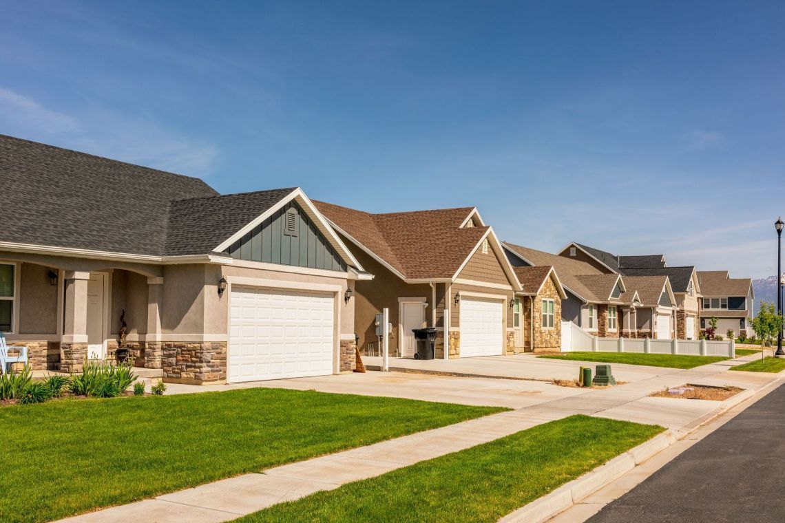 Row of houses with garages, green lawns, and a blue sky.