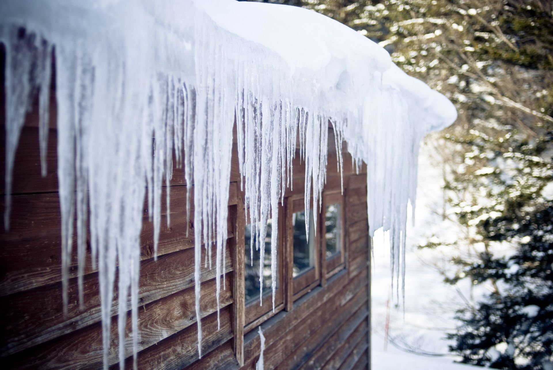 Brown wooden building with icicles hanging from the roof and snow on the ground.
