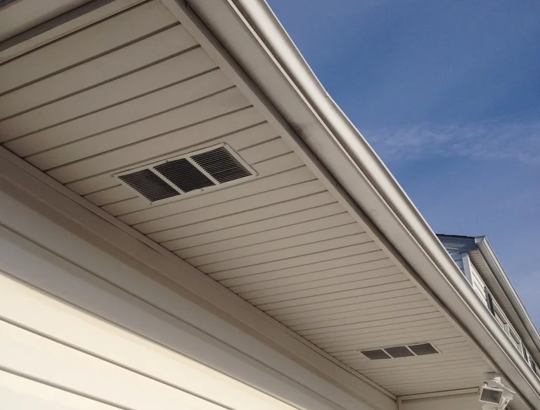 White soffit with vents and a gutter against a blue sky.