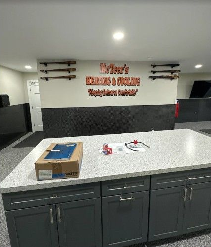 A kitchen island with a box on a granite countertop, in front of a wall with a McTeer's Heating & Cooling sign and decor.