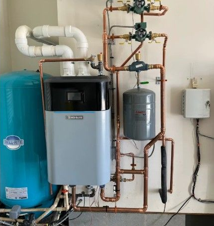 A wall-mounted boiler and water storage system with blue and gray tanks, copper piping, and white exhaust vents.